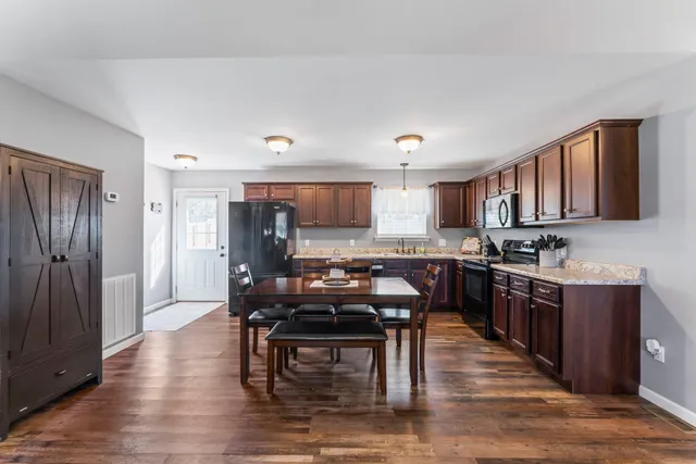 a kitchen with stainless steel appliances granite countertop a stove top oven a sink dishwasher a dining table and chairs with wooden floor