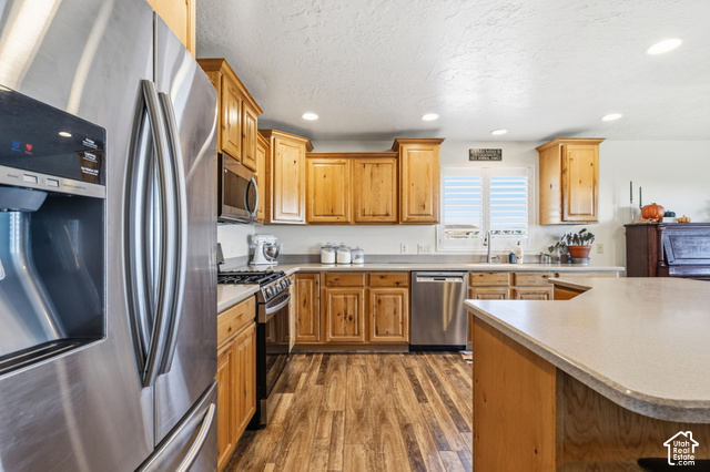 9044 North Cedar Pass Road Eagle Mountain, UT 84005 - Photo 13 of 63 Stainless steel appliances, wood-finish flooring, light wood cabinetry, recessed lighting, and a kitchen island with a light-toned countertop