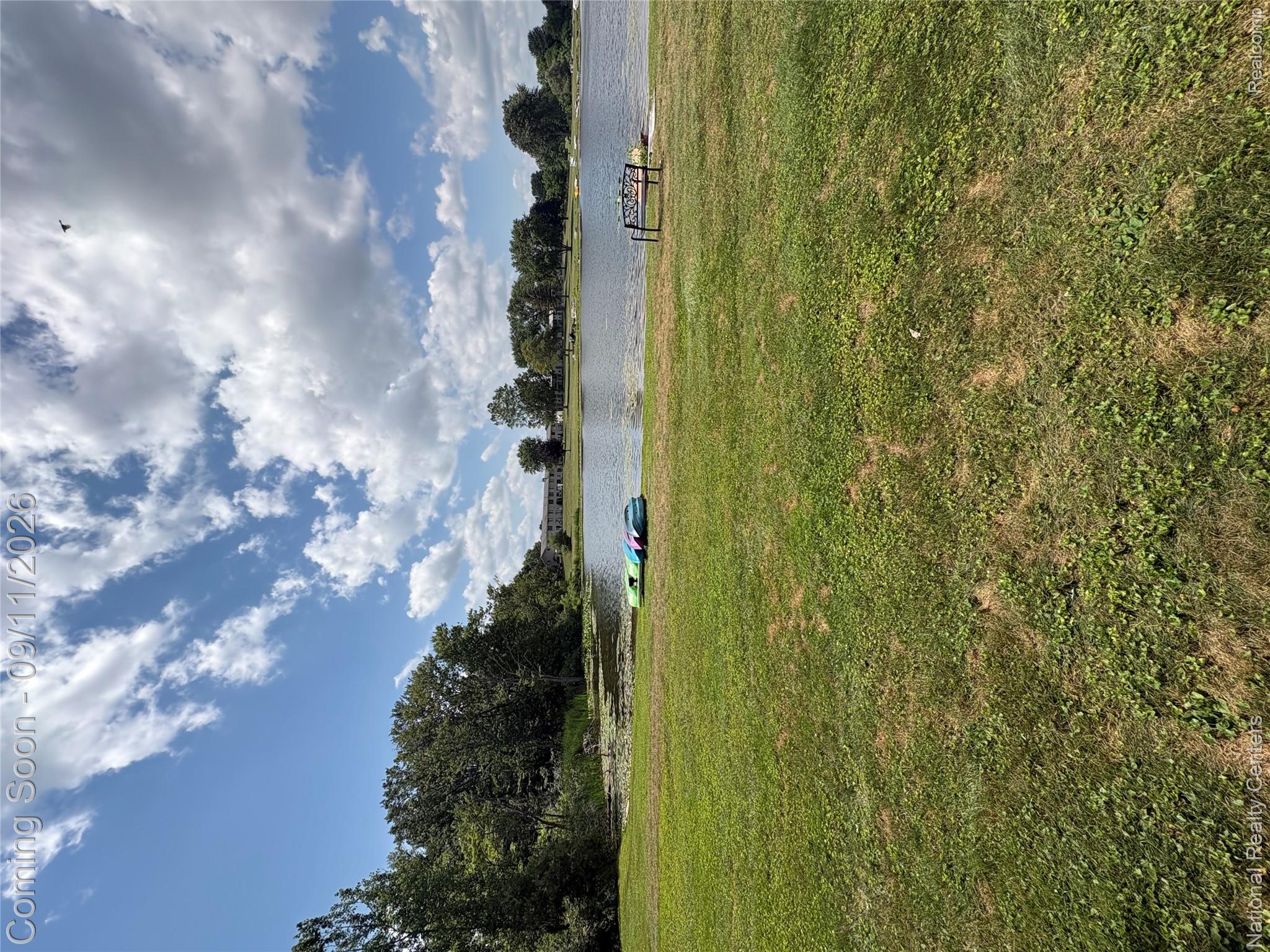 26945 Milford Road, Unit 3 New Hudson, MI 48165 - Photo 23 of 27 Lakefront grassed area with a wooden bench and distant structures
