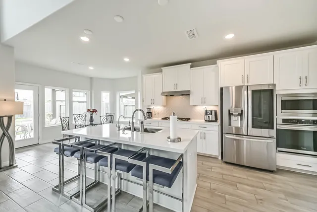 a kitchen with stainless steel appliances granite countertop a stove a refrigerator a sink a dining table and chairs