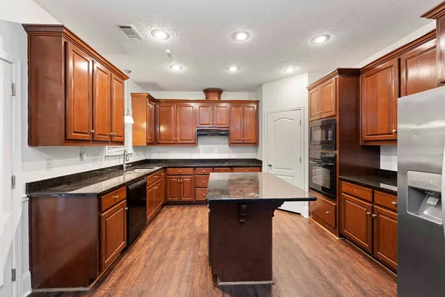 a kitchen with stainless steel appliances granite countertop wooden cabinets a stove top oven and granite counter tops with wooden floors