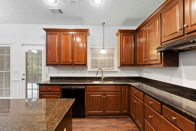 a kitchen with stainless steel appliances granite countertop wooden cabinets a sink and dishwasher a stove top oven with wooden floor