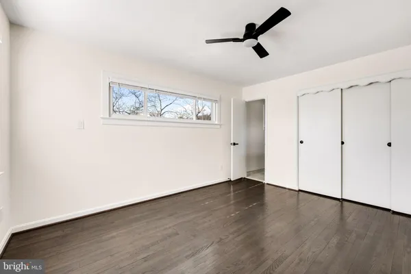 an empty room with wooden floor ceiling fan and windows