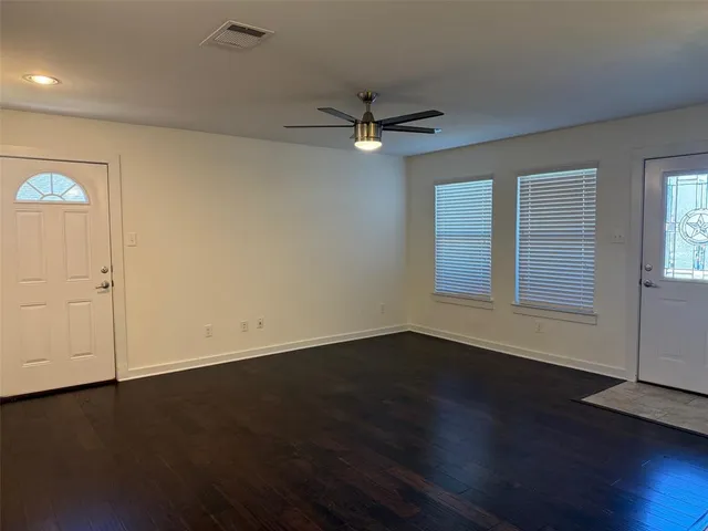 an empty room with wooden floor chandelier fan and windows