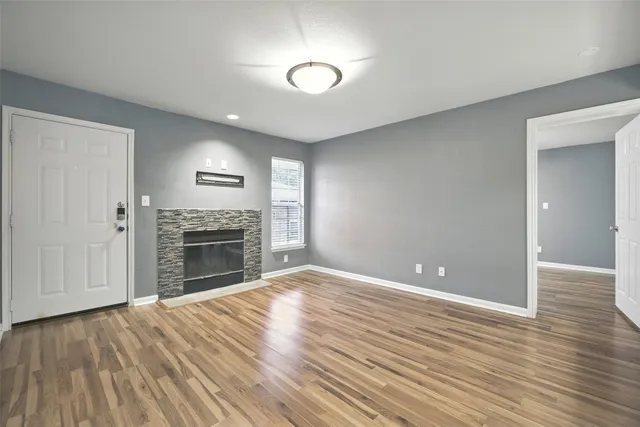 an empty room with wooden floor fireplace and windows