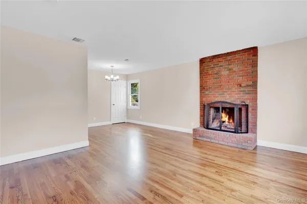 a view of an empty room with wooden floor fireplace and a window