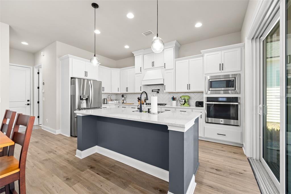 10778 Southwest 34th Road Gainesville, FL 32608 - Photo 16 of 62 a kitchen with kitchen island a sink a stove a refrigerator and white cabinets with wooden floor