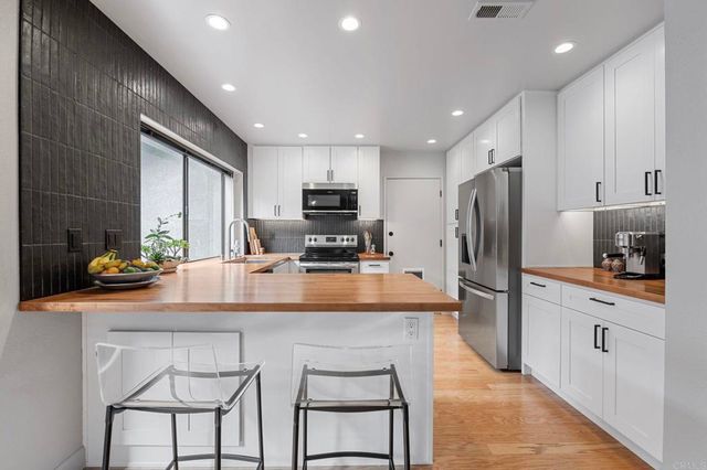 a kitchen with stainless steel appliances a sink a stove a refrigerator cabinets and a dining table with wooden floor