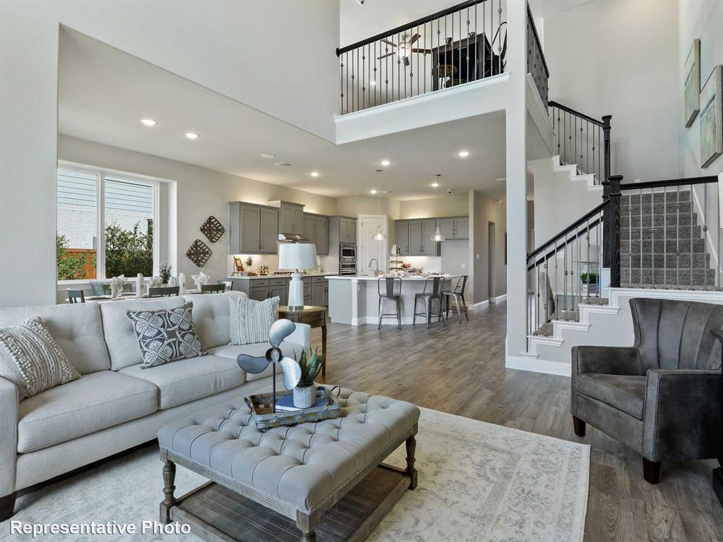 1143 Rothland Lane Red Oak, TX 75154 - Photo 3 of 18 Open-concept living area featuring high ceilings, wood-finish flooring, a two-story staircase with wrought iron balusters, a kitchen with grey cabinetry and an island, and a dining area with ample natural light