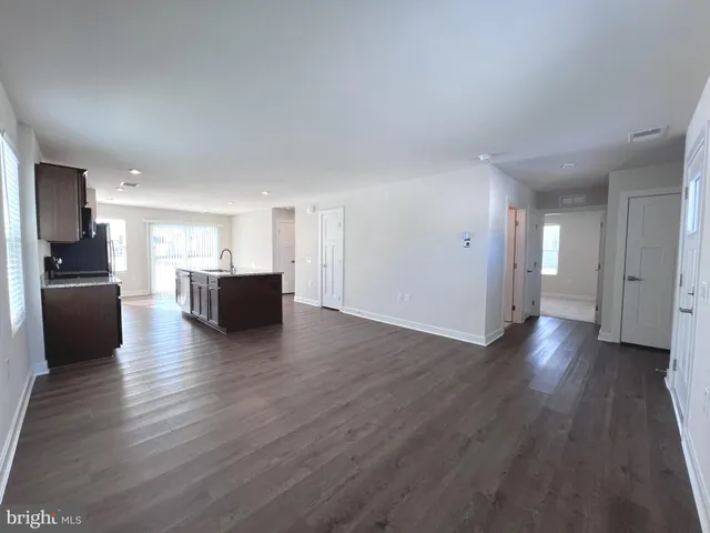a view of an empty room with wooden floor and a kitchen