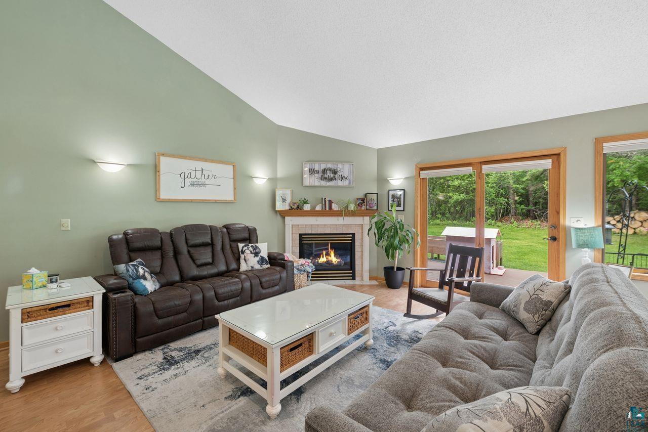 202 Prentice Heights Road Ashland, WI 54806 - Photo 2 of 28 Living room featuring vaulted ceilings, wood-finish flooring, a fireplace with a light-toned mantel, sconce lighting, and a glass-paneled patio door opening to outdoor space