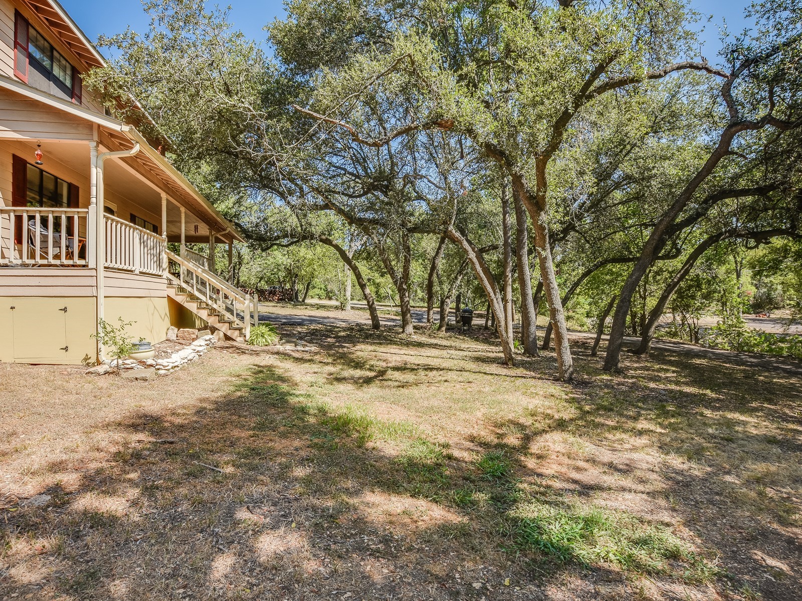 13404 Cedar Lime Road Leander, TX 78641 - Photo 6 of 28 A charming home with a broad, inviting porch is nestled among mature trees, offering ample shade and natural beauty.