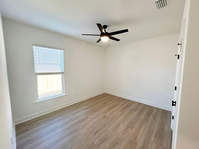 a view of empty room with wooden floor and fan