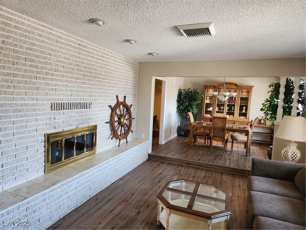 2645 South Lindell Road Las Vegas, NV 89146 - Photo 5 of 30 Living room featuring a textured ceiling, a brick fireplace, wood finished floors, and brick wall