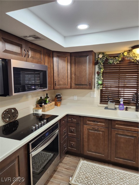 2645 South Lindell Road Las Vegas, NV 89146 - Photo 8 of 30 Kitchen with oven, stovetop, light wood-style flooring, dark brown cabinetry, and light countertops