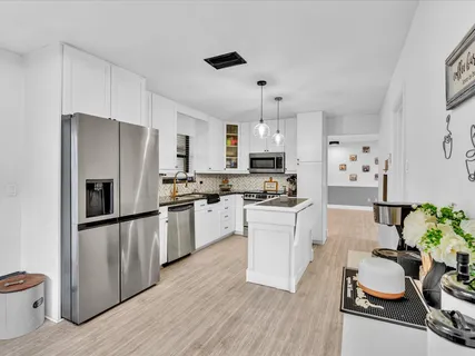 a kitchen with stainless steel appliances a refrigerator a stove a sink dishwasher and white cabinets with wooden floor