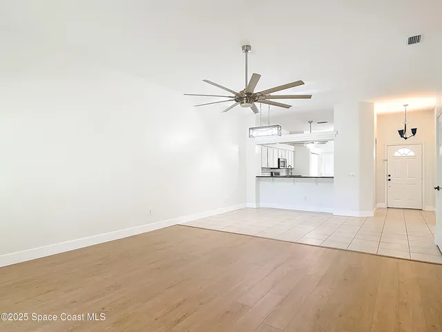 an empty room with wooden floor chandelier fan and windows