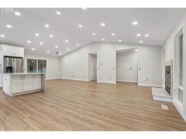 a view of an empty room with wooden floor and kitchen