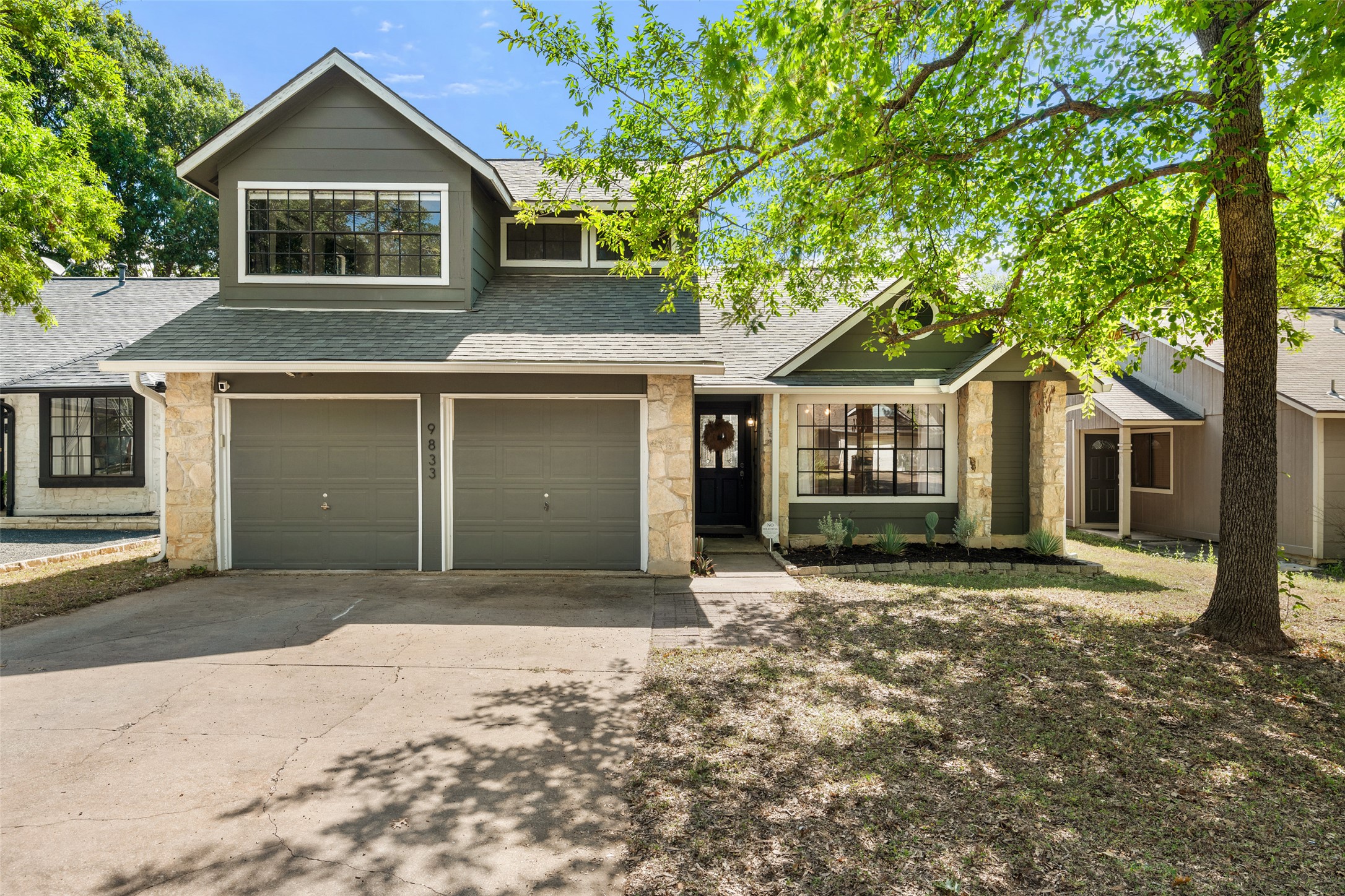 Traditional-style home with stone siding, a shingled roof, a garage, and driveway