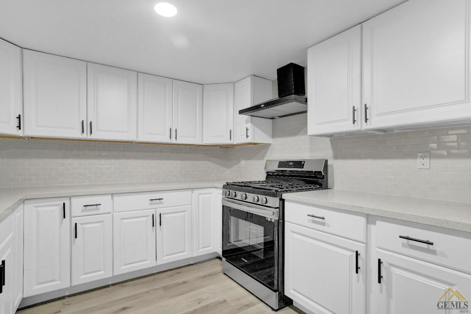 Undisclosed Address Bakersfield, CA 93304 - Photo 11 of 32 a kitchen with white cabinets and a stove with wooden floor