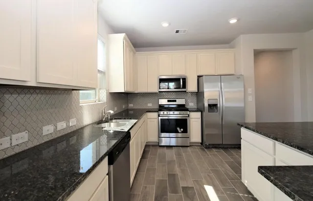 a kitchen with granite countertop a refrigerator oven a sink dishwasher and white cabinets with wooden floor