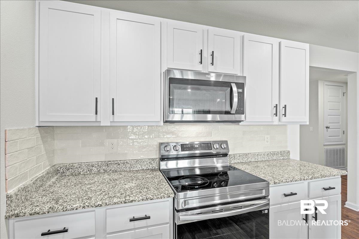 23641 Unbridled Loop Daphne, AL 36526 - Photo 9 of 40 White shaker-style cabinetry with matte black hardware, stainless steel microwave, electric range, and granite-style countertops