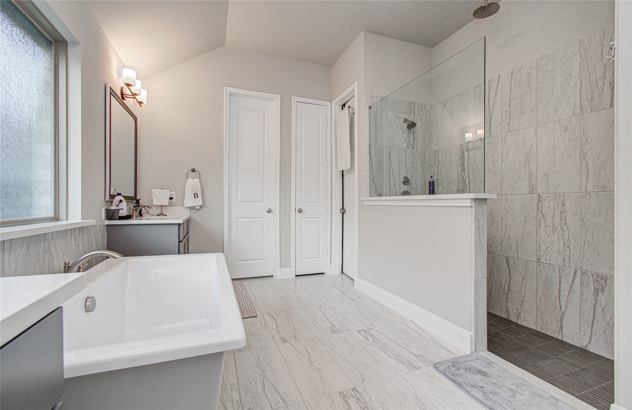 17344 Grand Canyon Road Conroe, TX 77302 - Photo 27 of 49 This bathroom features a modern design with a spacious walk-in shower, a sleek freestanding bathtub, and dual sinks with large mirrors. The neutral color palette and ample natural light create a clean and inviting atmosphere.