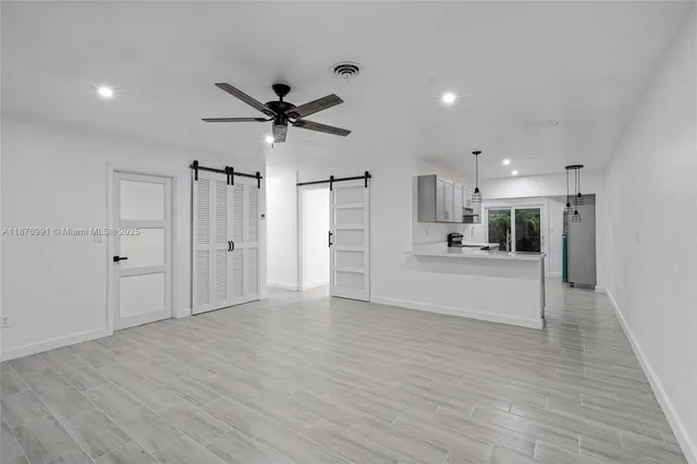 a view of an empty room and kitchen view with wooden floor