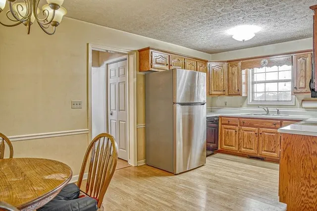 a kitchen with stainless steel appliances granite countertop a refrigerator a sink dishwasher a dining table and chairs with wooden floor