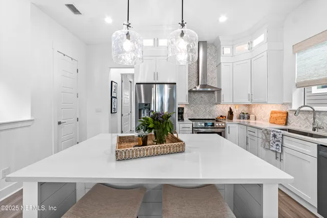 a kitchen with stainless steel appliances kitchen island granite countertop a refrigerator a stove a sink dishwasher and white cabinets with wooden floor