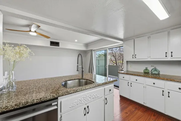 a kitchen with granite countertop a sink stainless steel appliances white cabinets and wooden floor