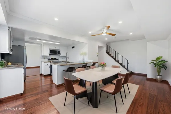 a white kitchen with stainless steel appliances kitchen island a table and chairs in it
