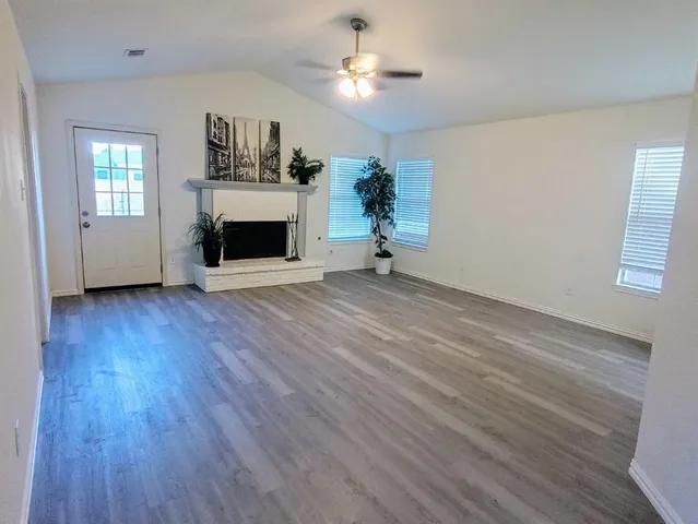 an empty room with windows a fireplace and a ceiling fan