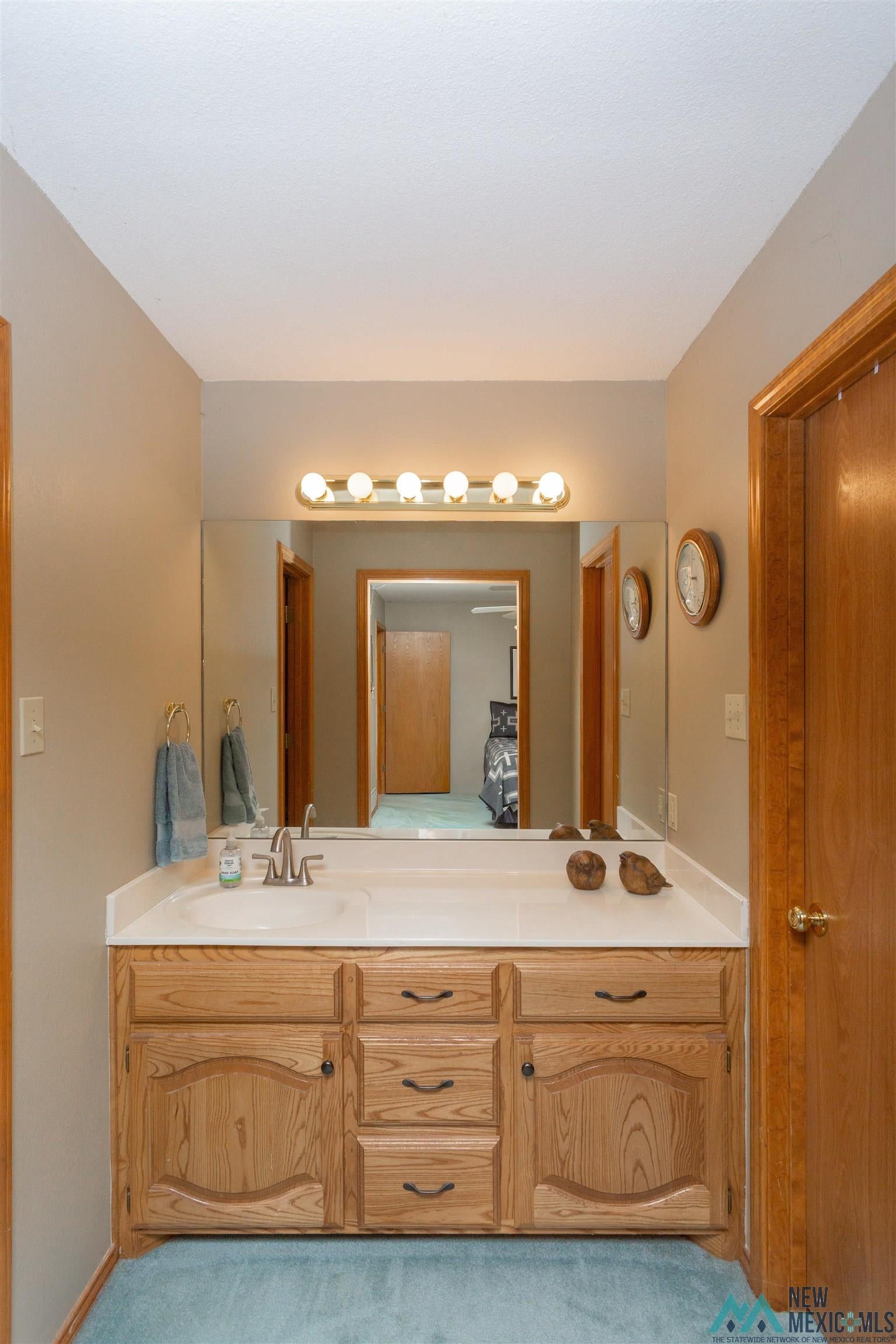 2012 South Haldeman Road Artesia, NM 88210 - Photo 29 of 96 Vanity area featuring a wood-finish cabinet with multiple drawers and doors, a white countertop with an integrated sink, and a large wall-mounted mirror