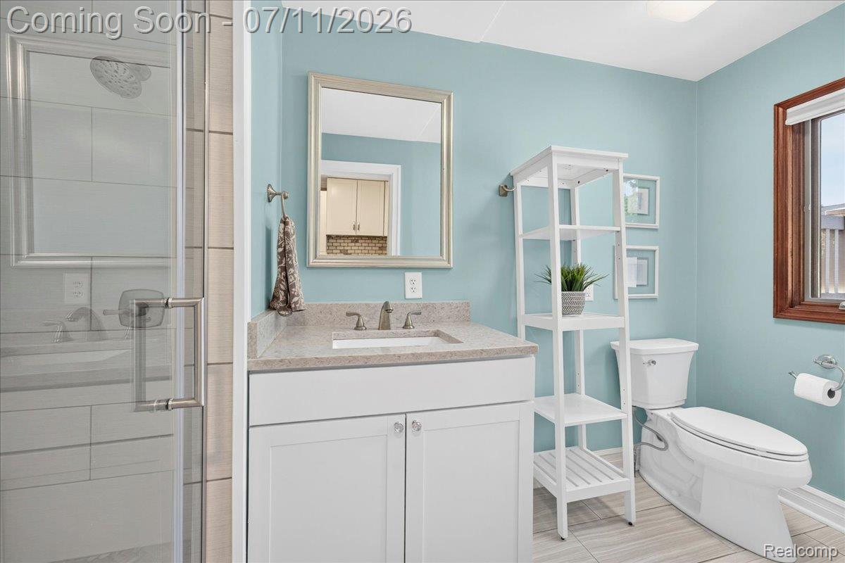 23750 East River Road Grosse Ile, MI 48138 - Photo 16 of 54 Bathroom featuring a glass-enclosed shower, white vanity with a light-colored countertop, and a window with wood trim