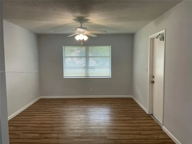an empty room with wooden floor chandelier fan and windows