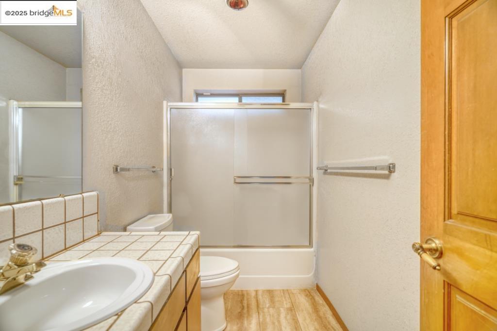 19195 Ferretti Road Groveland, CA 95321 - Photo 24 of 51 Bathroom featuring a textured wall, vanity, light wood-style flooring, bath / shower combo with glass door, and a textured ceiling