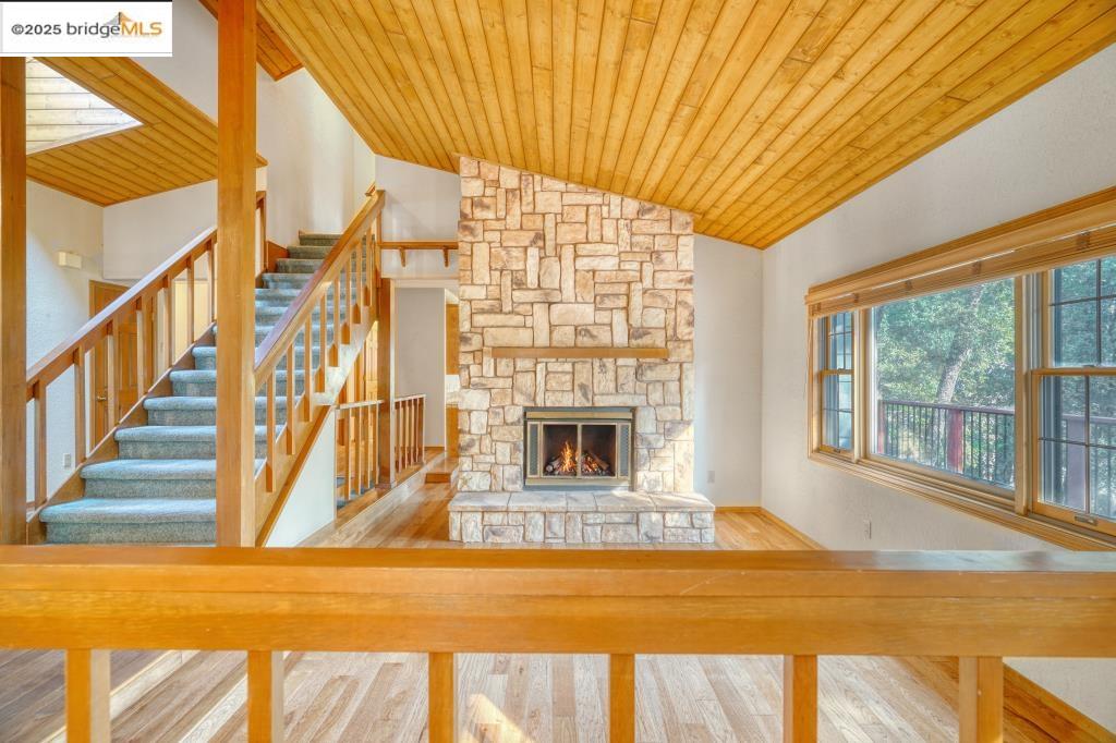19195 Ferretti Road Groveland, CA 95321 - Photo 9 of 51 Unfurnished living room featuring a stone fireplace, lofted ceiling, wood finished floors, wooden ceiling, and stairway