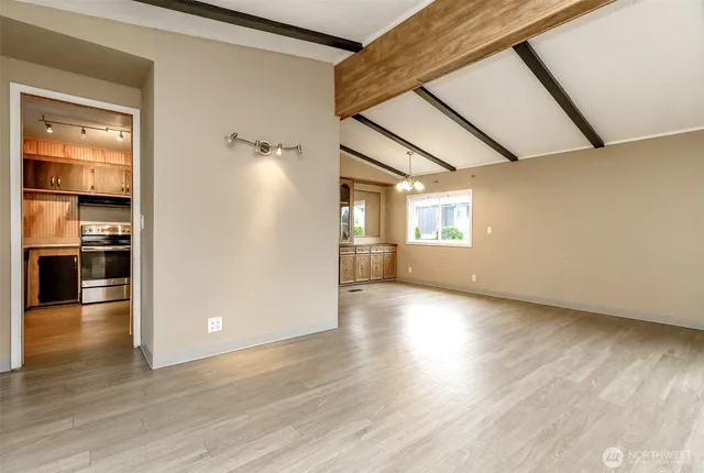 an empty room with wooden floor kitchen view and windows