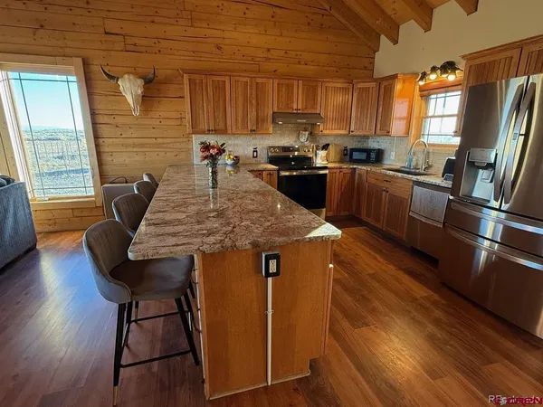 a kitchen with stainless steel appliances granite countertop a stove a refrigerator a sink a dining table and chairs with wooden floor