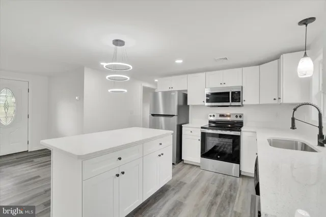 a large white kitchen with stainless steel appliances granite countertop a stove a sink dishwasher and a refrigerator with wooden floor