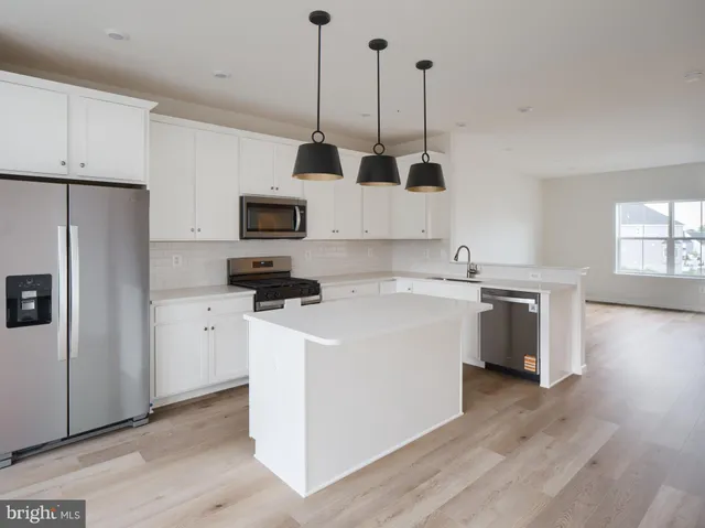 a kitchen with stainless steel appliances granite countertop a stove top oven a sink a refrigerator and white cabinets with wooden floor