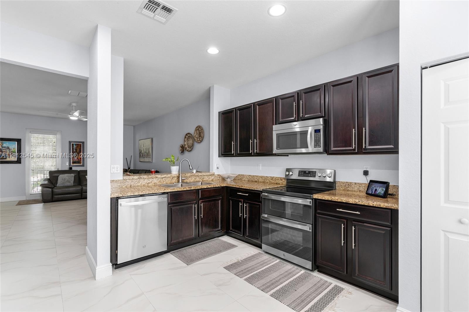 2565 Southwest 119th Terrace Miramar, FL 33025 - Photo 14 of 37 a kitchen with stainless steel appliances granite countertop a stove top oven a sink dishwasher a refrigerator and a microwave oven with wooden floor