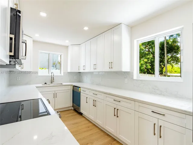 a kitchen with a sink dishwasher a stove and white cabinets with wooden floor