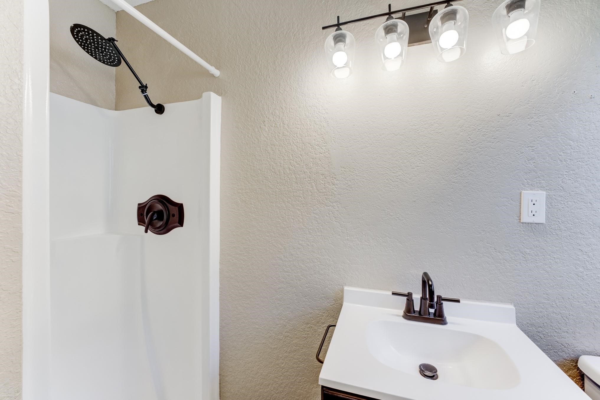 305 Yaupon Street Sweeny, TX 77480 - Photo 20 of 22 Compact bathroom featuring a modern shower with a rainfall showerhead, a sleek vanity with a single sink, and stylish lighting fixtures.