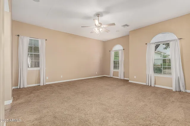 an empty room with chandelier fan and windows
