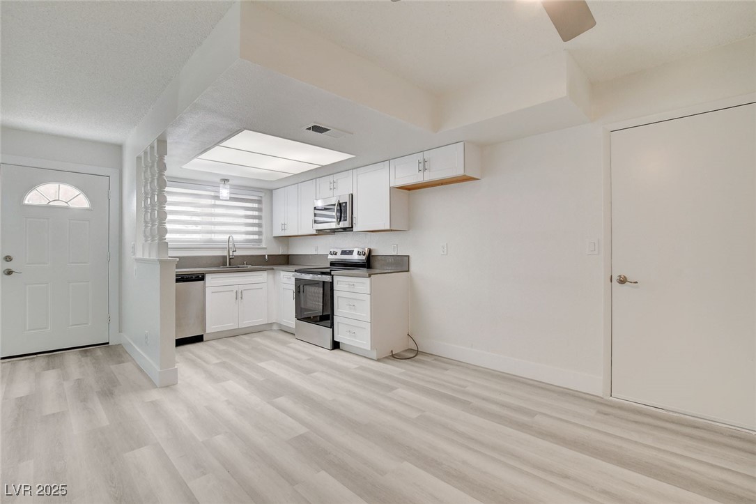579 Roxella Lane, Unit B Las Vegas, NV 89110 - Photo 11 of 28 Kitchen featuring white cabinets, appliances with stainless steel finishes, light wood-style flooring, and dark countertops