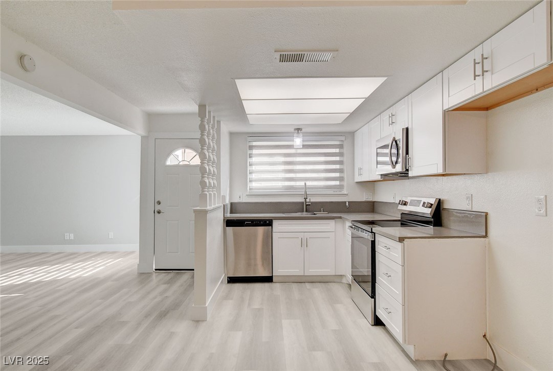 579 Roxella Lane, Unit B Las Vegas, NV 89110 - Photo 13 of 28 Kitchen with stainless steel appliances, white cabinets, light wood-style floors, a textured ceiling, and pendant lighting