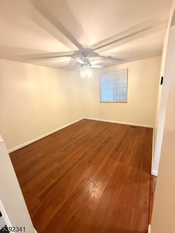 a view of empty room with wooden floor and fan