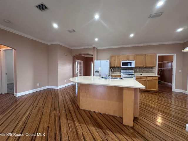 a living room with stainless steel appliances furniture wooden floor and a kitchen view